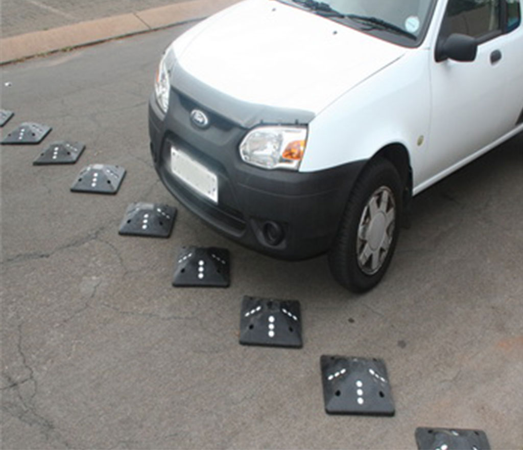 Black square speed bumps with white markings on the road for traffic-calming purposes.