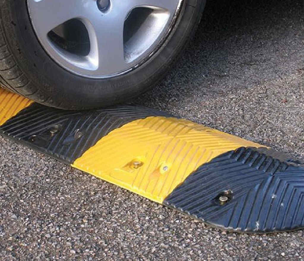A car is about to pass over a black and yellow road bump.