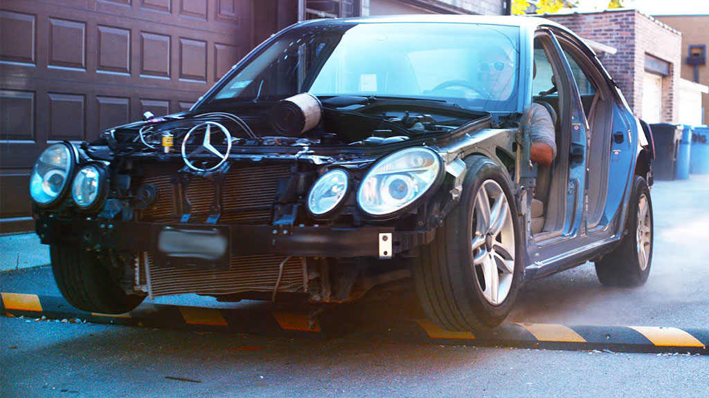 A black Mercedes is about to pass over a black and yellow speed bump.