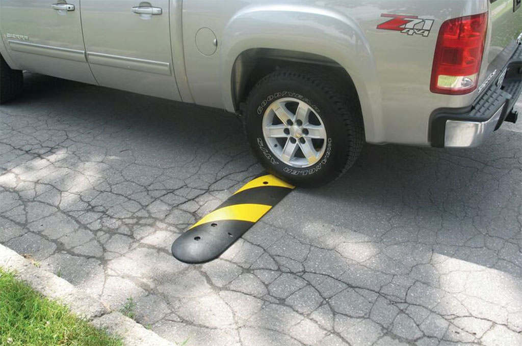 A black and yellow speed bump mounted on the road to reduce speed.