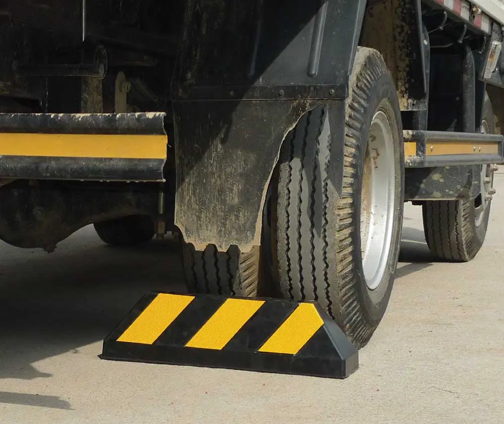 A black wheel stop with yellow reflective films helps a heavy-duty vehicle to park.