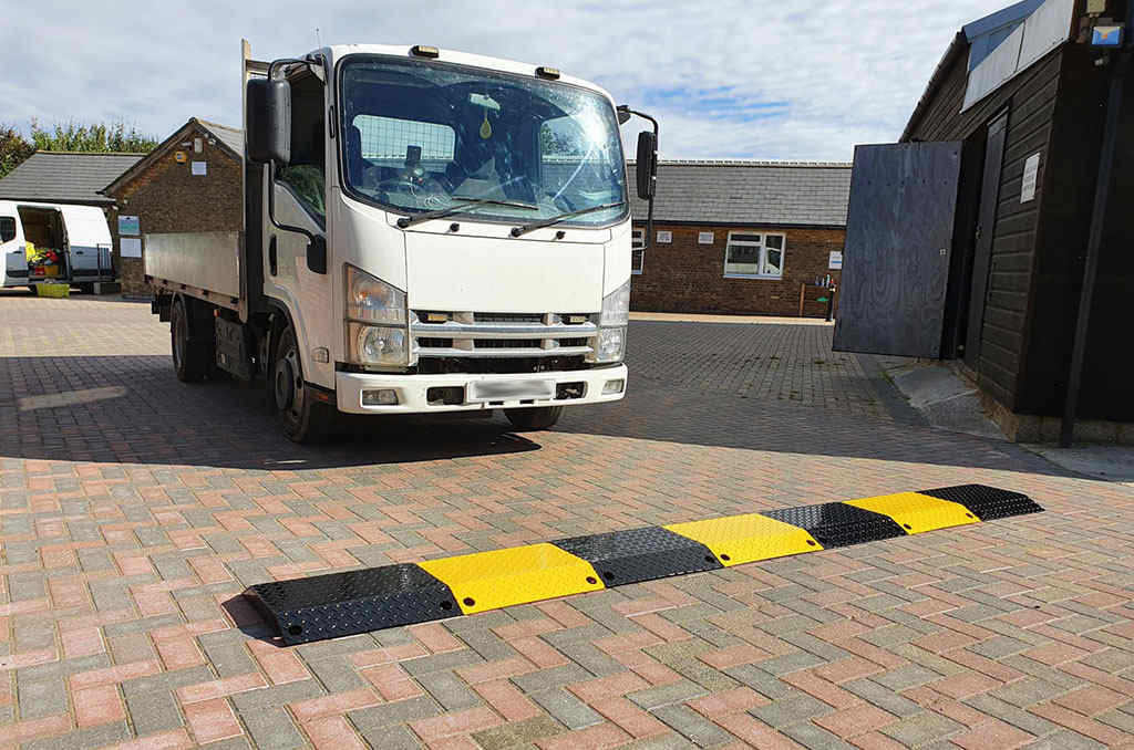 A white heavy-duty vehicle is about to pass over a black and yellow metal speed bump.