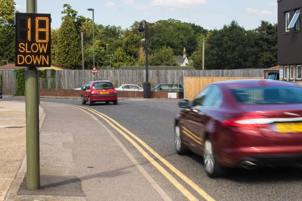 A red car approached the radar speed sign, which displayed "18" and "slow down".