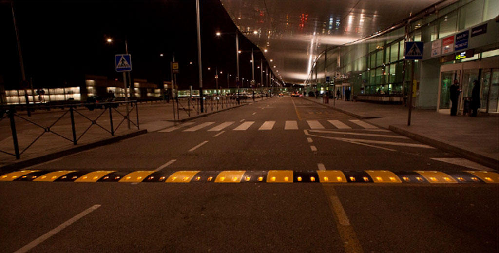 A black and yellow speed bump with lights at night to increase visibility.