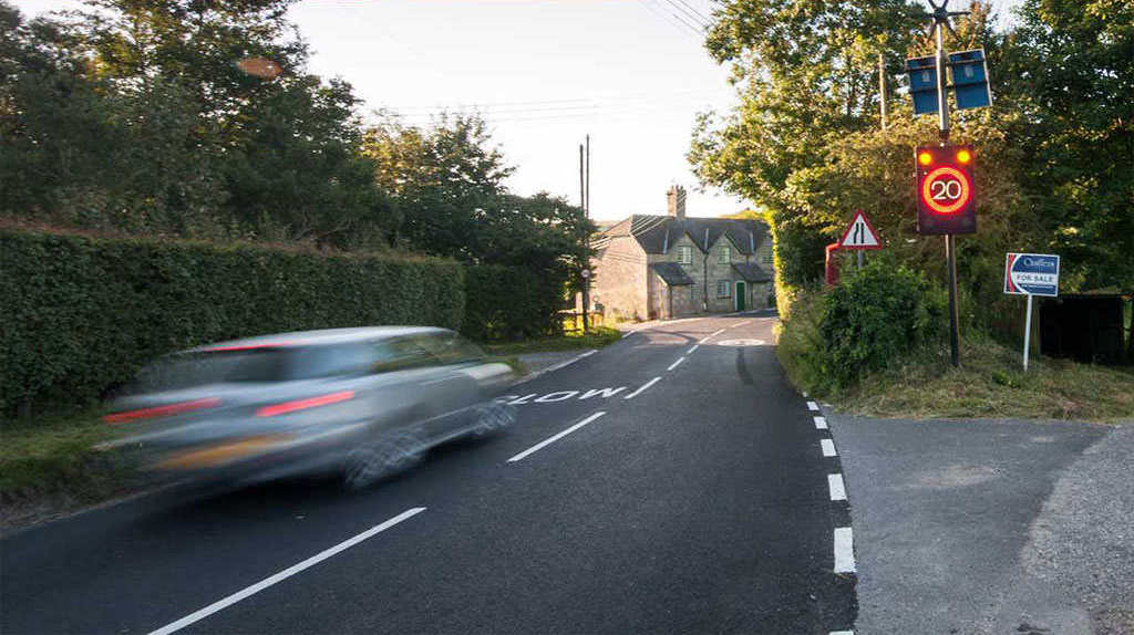 A speed limit sign and a road narrowing traffic sign along the road.