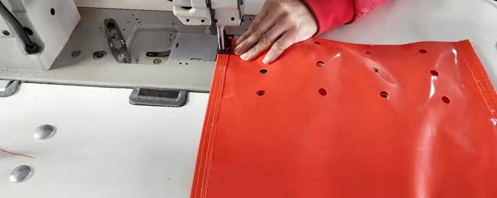 A worker is doing the sewing process for an orange sandbag which is made of PVC material for traffic management purposes.