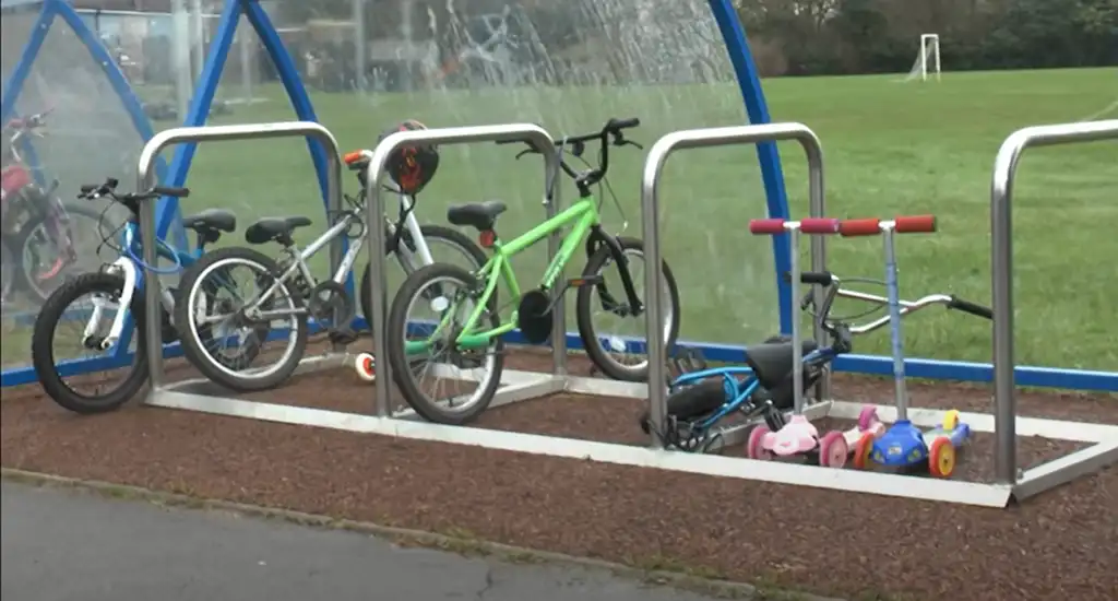A Sheffield-style bicycle rack with several children's bicycles parked on it.