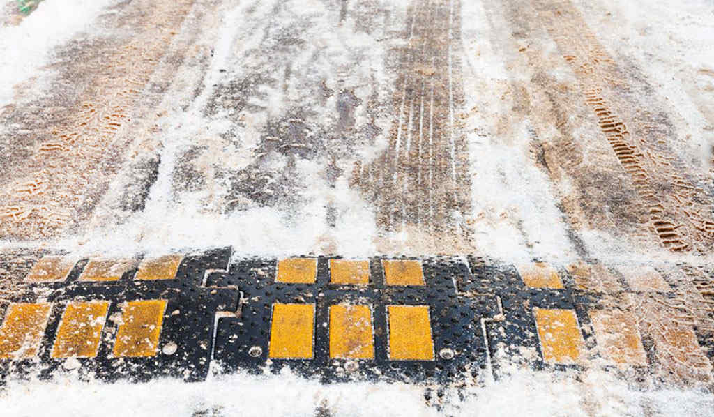 A black speed bump with yellow strips in snowy weather.