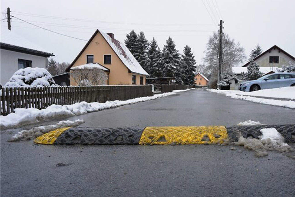 A black and yellow speed bump on a snowy road.