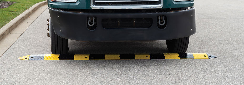 A car is about to pass over a black and yellow road bump made of steel.