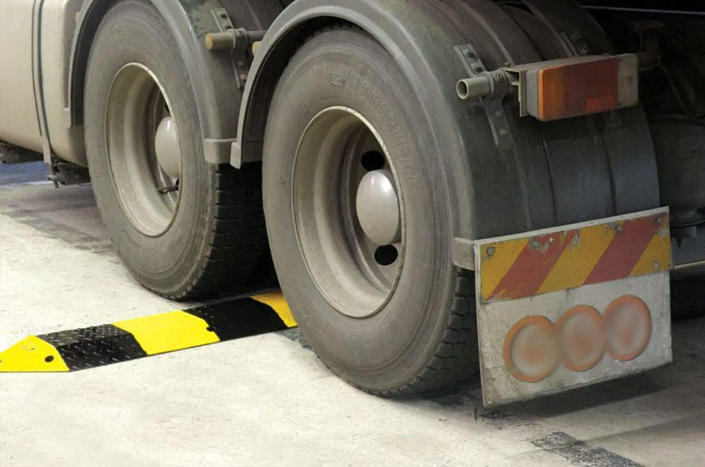 A heavy-duty vehicle is about to pass a black and yellow steel speed bump.