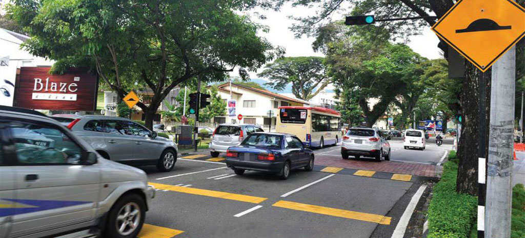 Several cars and a traffic speed bump of black and yellow on the road.