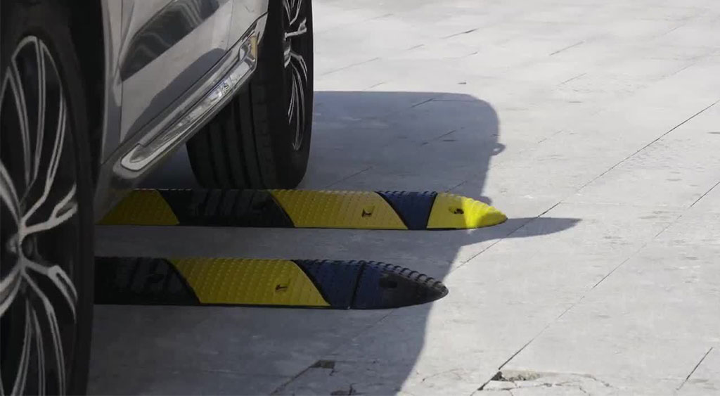 Rear wheels of a black car are about to pass over two black and yellow speed bumps.