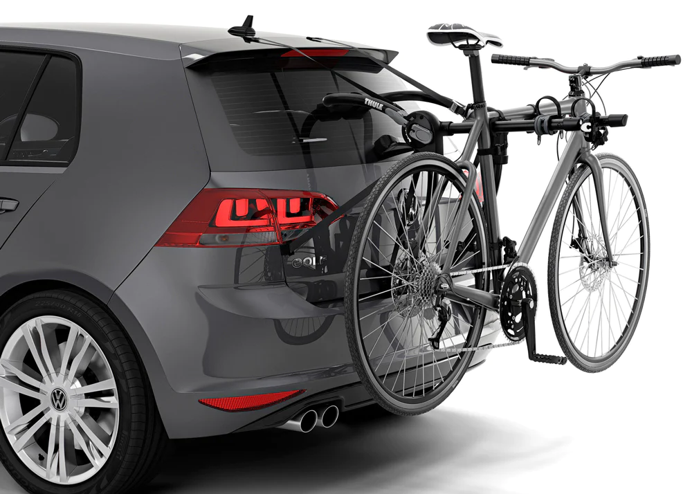 A bicycle is mounted onto the rear of a black car with the assistance of a trunk-mounted bicycle rack.