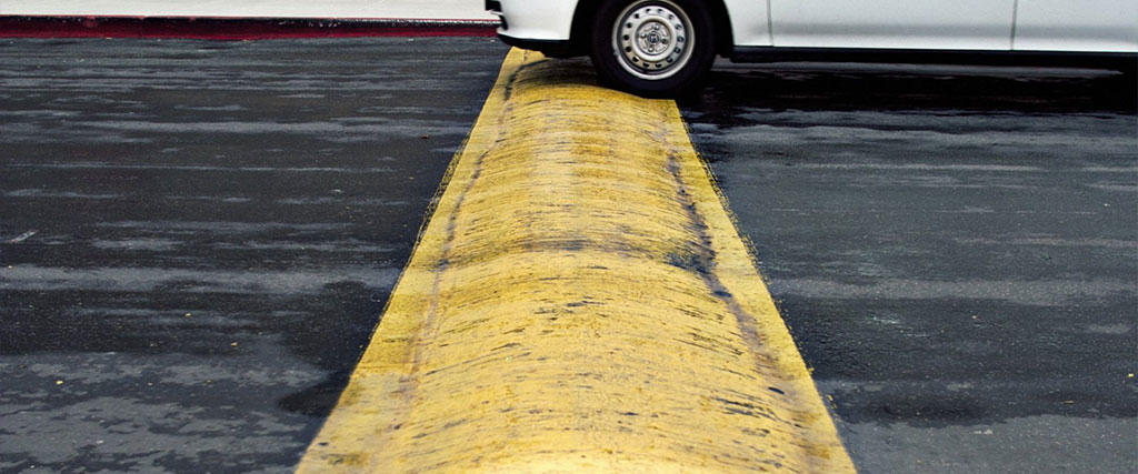 A white car is about to pass over a yellow speed bump.